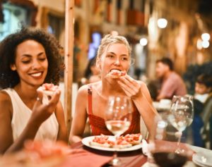 Two women eat Italian food and drink wine at a busy restaurant.